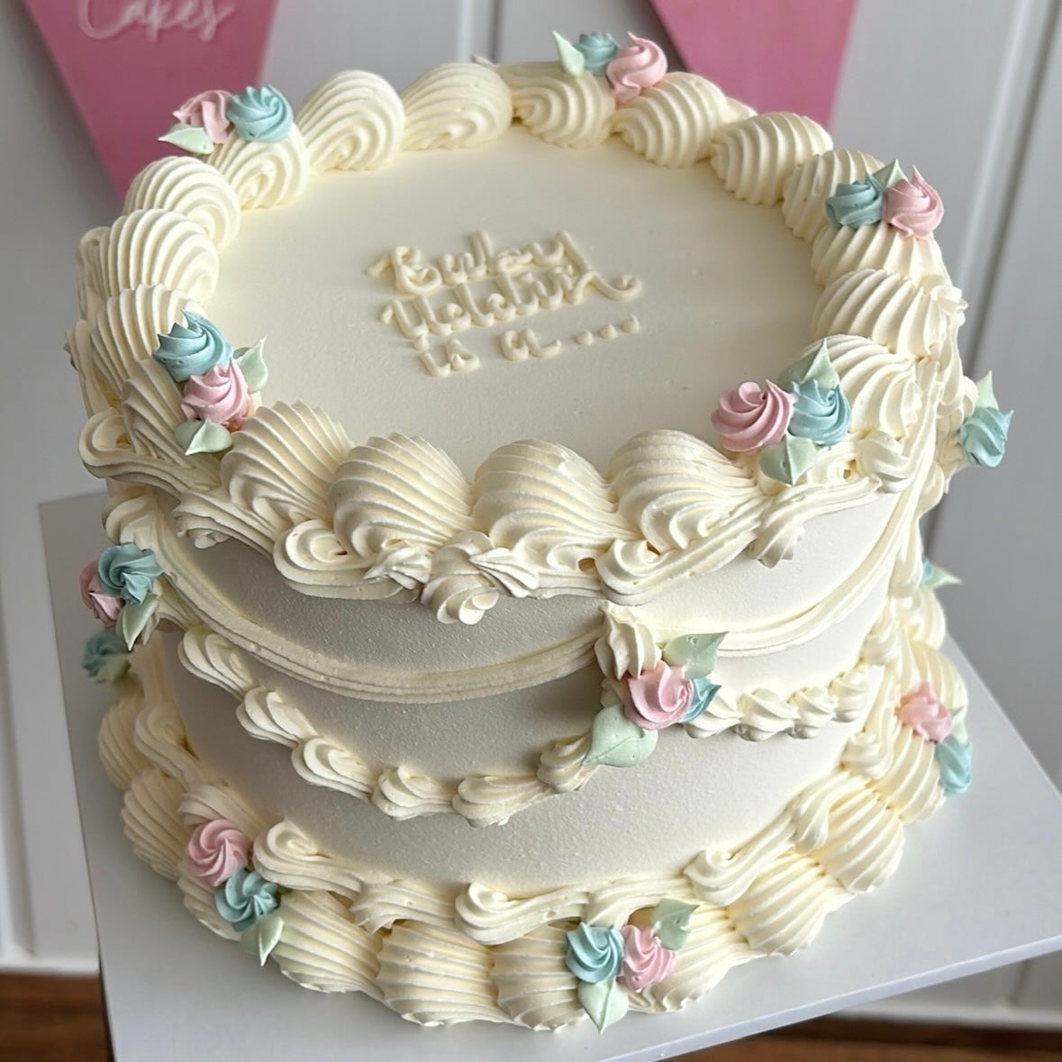 Gender reveal cake with smooth white icing, decorated with swirls of pink and blue buttercream. A small topper reads ‘Boy or Girl?’, ready for the reveal.