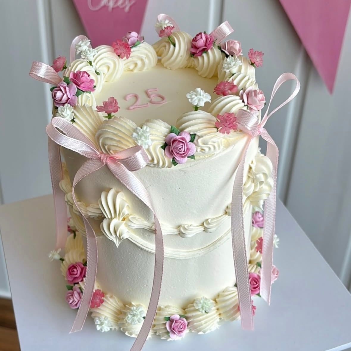 Elegant white vintage-style cake decorated with artificial pink gypsophila, mini rose heads in shades of pink, and pale pink satin bows.